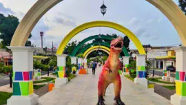 Descripción de la foto para personas con discapacidad visual: Paseo al aire libre con arcos de colores y una persona disfrazada de dinosaurio. (Créditos: Villa Hermosa Petapa)