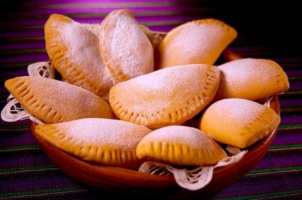 Descripción de foto - empanadas espolvoreadas con azúcar glas, puesta sobre una mesa decorada con un mantel típico. - Crédito de foto - Molinos Modernos