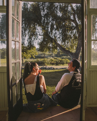 Descripción de foto - Un hombre y una mujer riéndose en la entrada de su casa con un paisaje natural. - Crédito de foto - @jmvillejo