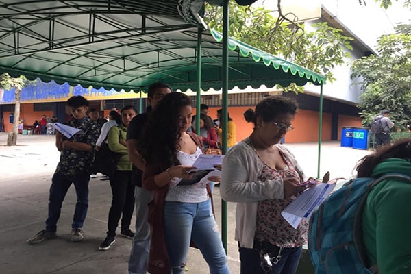 Descripción de la foto - Estudiantes de la USAC haciendo cola, mientras esperan y leen el boletín - Crédito Universidad de San Carlos de Guatemala 2.0