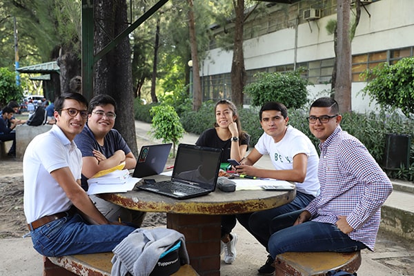 Descripción de la foto estudiantes de la USAC sentados en las afueras de las instalaciones estudiando - Crédito Soy Usac
