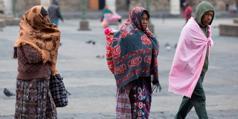 Descripción de foto - dos mujeres y un hombre abrigados con chamarras y telas mientras caminan por el parque central. - Crédito de foto - DCA