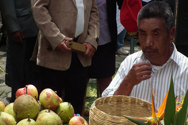 Descripción de foto - hombre vendiendo peras y manzanas durante una procesión en San Bartolomé Milpas Altas. - Crédito de foto - Chapín AC