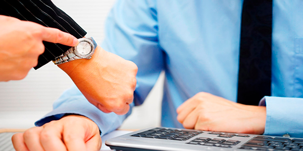 Descripción de foto - Mano de mujer, señalando su reloj de mano, a un hombre que está sentado frente a su escritorio. - Crédito de foto - La 100 Cineradios