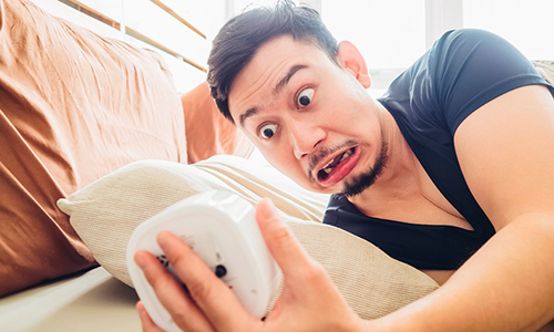 Descripción de foto - hombre acostado en su cama, asustado, viendo un reloj. - Crédito de foto - Emol Pyme