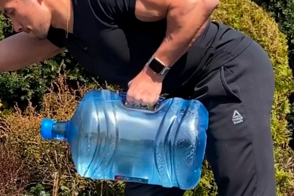 Descripción de foto - hombre levantando un tambo de agua pura con un brazo. - Crédito de foto - MSN