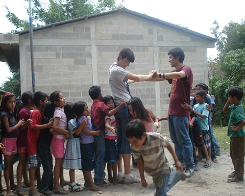 Descripción de la foto para personas con discapacidad visua - Niños jugando con adultos y pasando por debajo de la campana. - Crédito de foto - Grace in Guatemala