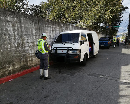 Descripción de la foto para personas con discapacidad visual - Agente de emetra colocando una multa por estacionarse en línea roja.- Departamento de Tránsito de la Policía Municipal