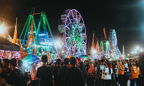 Descripción de la foto para personas con discapacidad visual - Personas caminando por la noche en una feria patronal. - Crédito de foto - Forum Guatemala