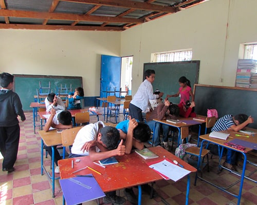 Descripción de la foto para personas con discapacidad visual - niños en un salón, recostados boja abajo con la mano levantada. - Crédito de foto - Chicos and Kid Inc